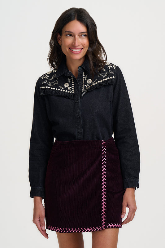 Woman wearing a black embroidered top and maroon skirt on a white background
