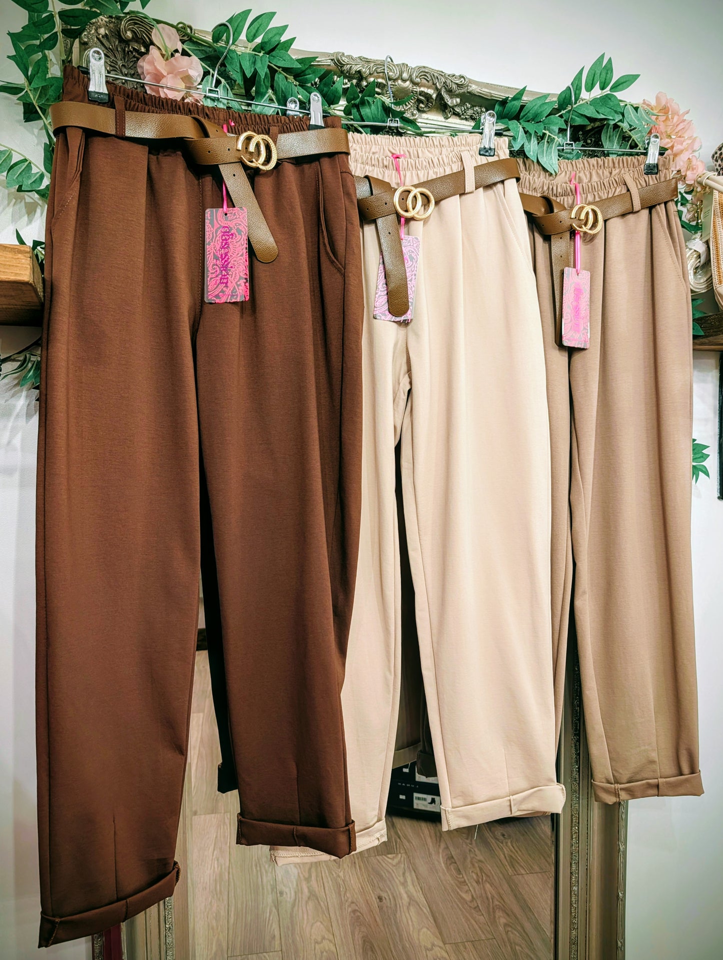 Three pairs of pants hanging on a mirror. One brown and one beige and one camel