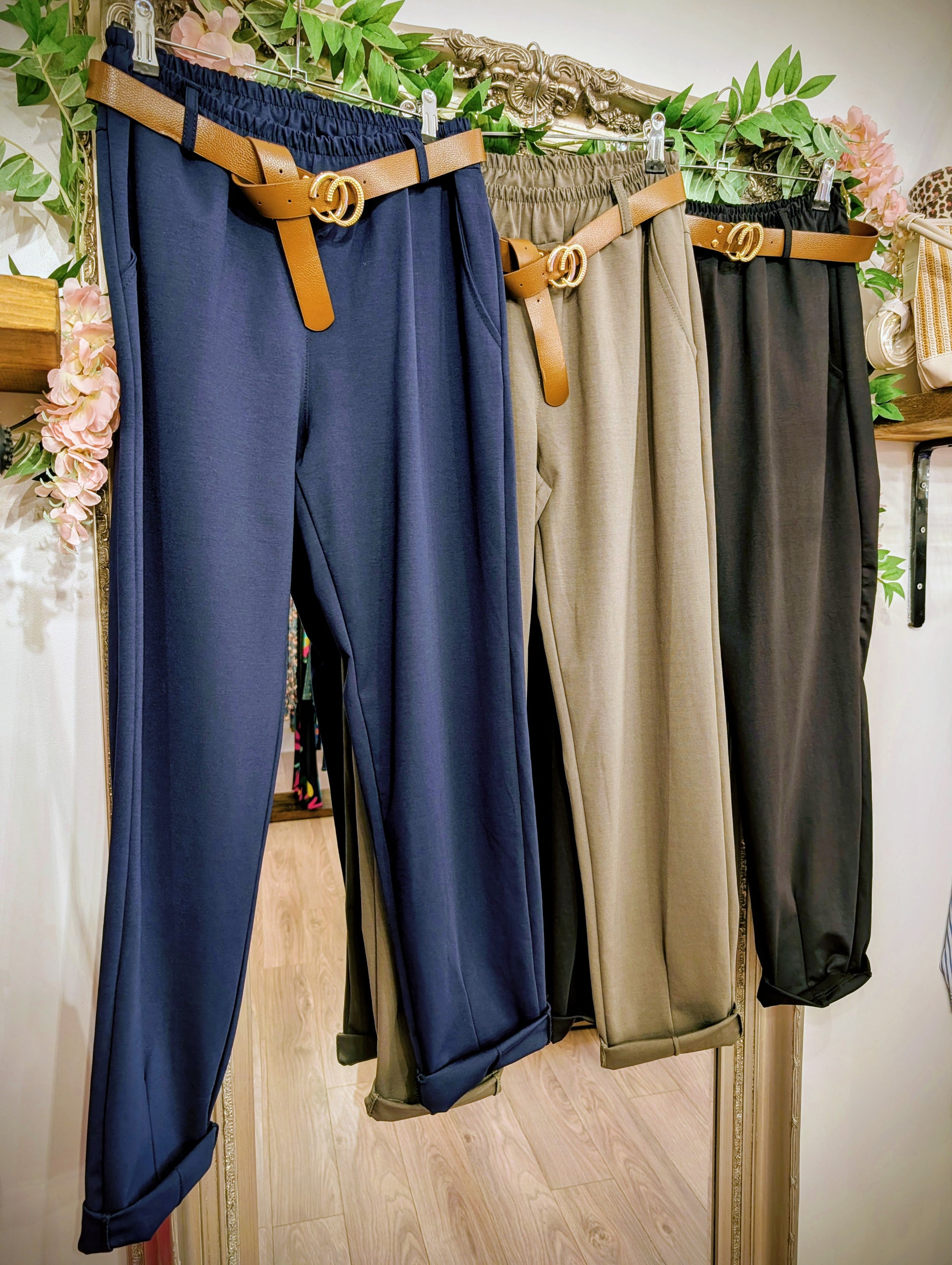 Three pairs of pants in blue, beige, and black hanging on a rack with a belt.