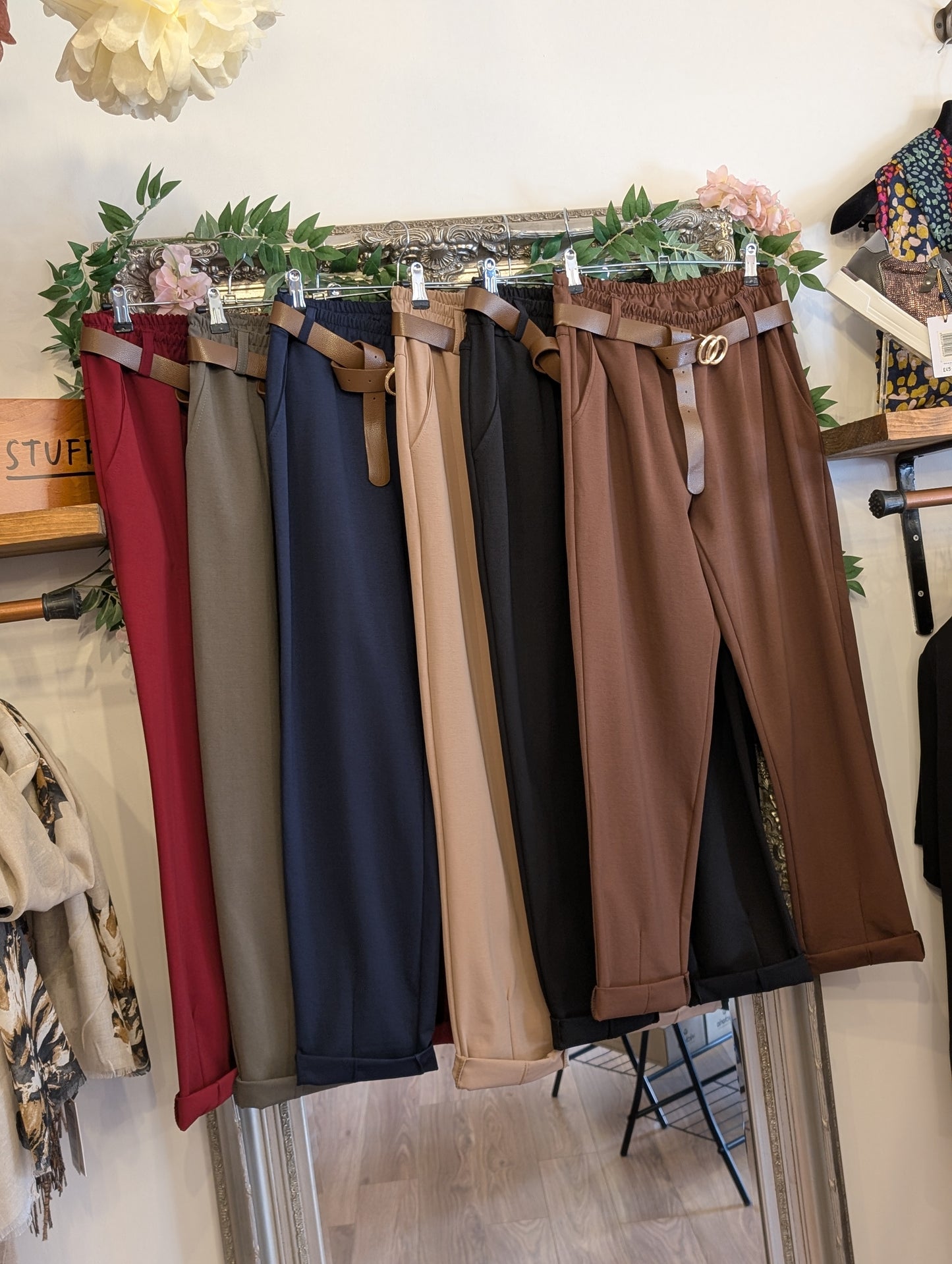 Set of pants in various colors hanging on a rack with a store interior background.