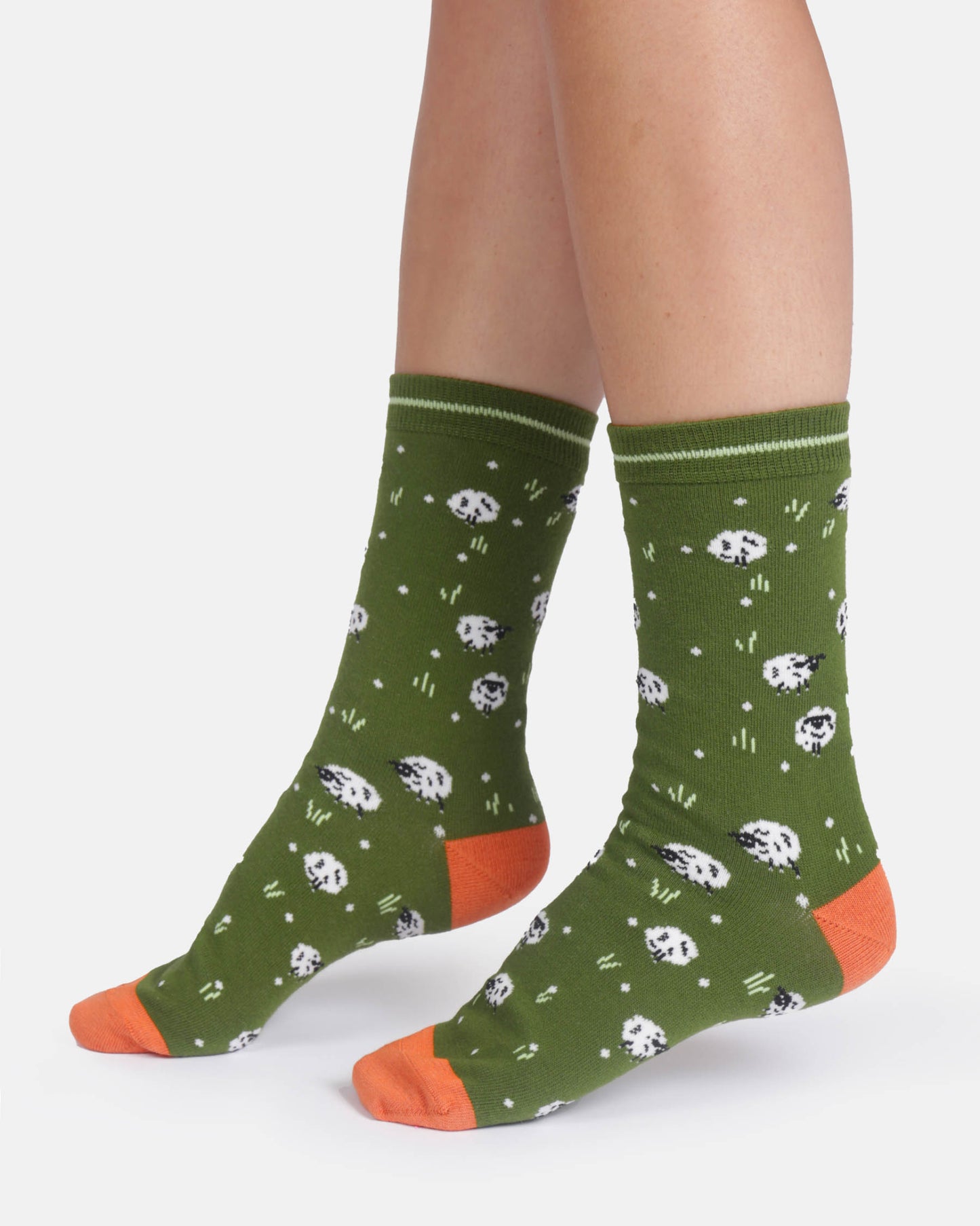 Green socks with white sheep patterns and orange toes worn by a person on a white background