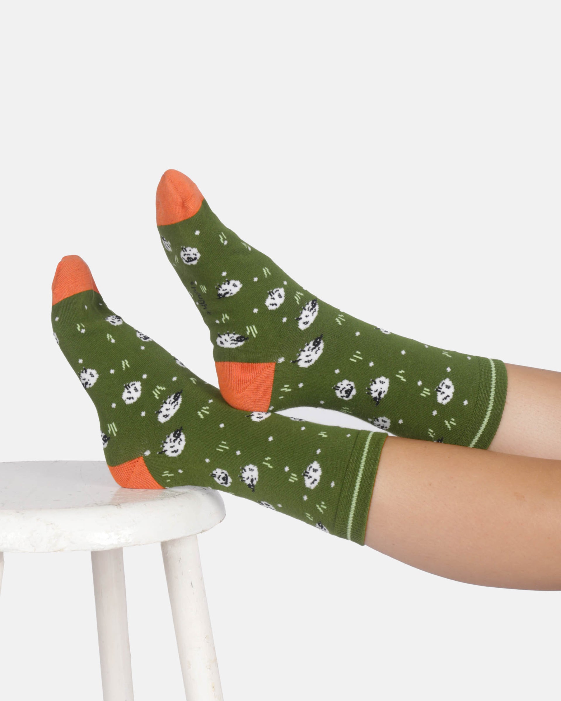 Green socks with white patterns and orange accents worn by a person sitting on a white stool.