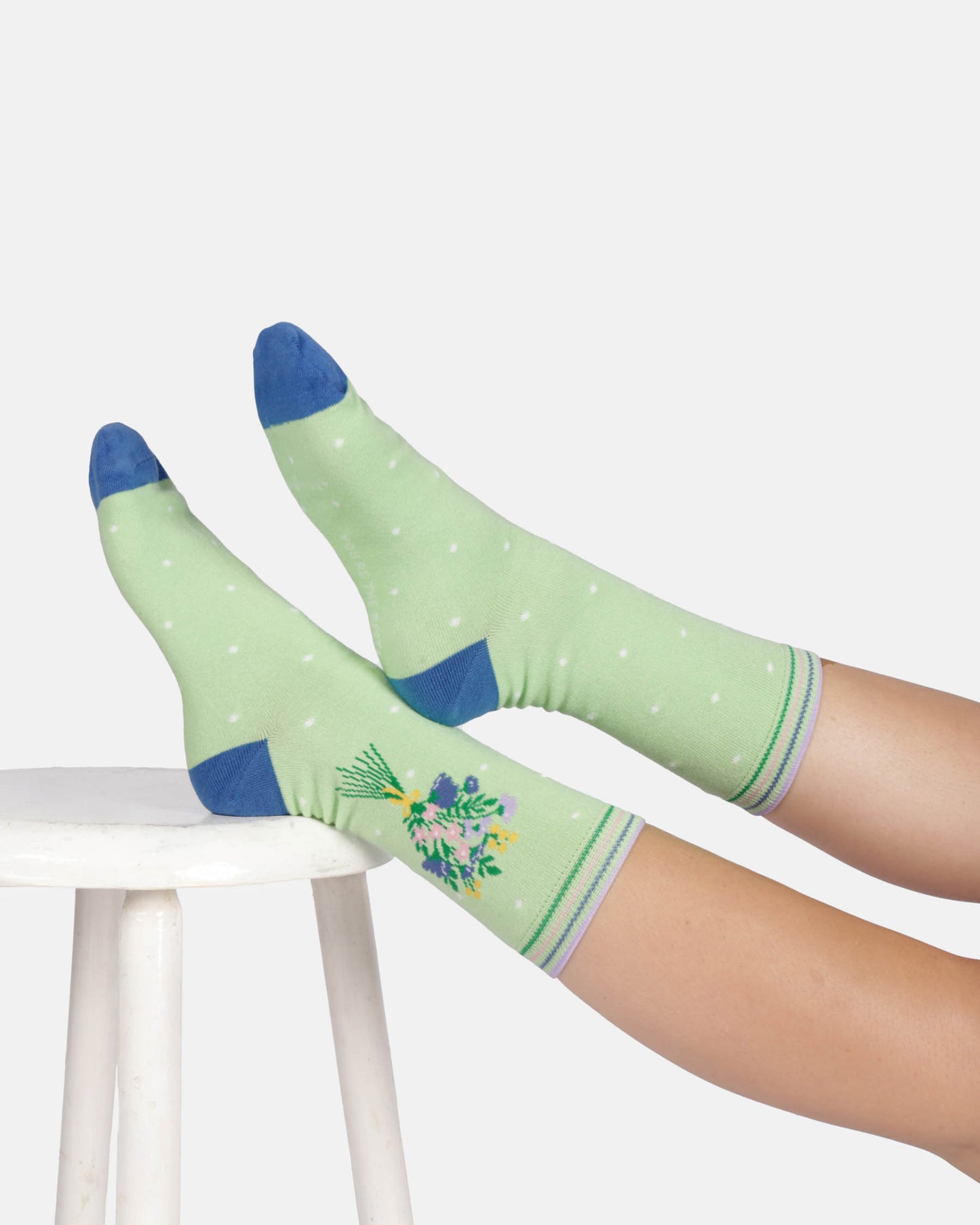 Green socks with blue toes and cuffs worn by a person sitting on a white stool.