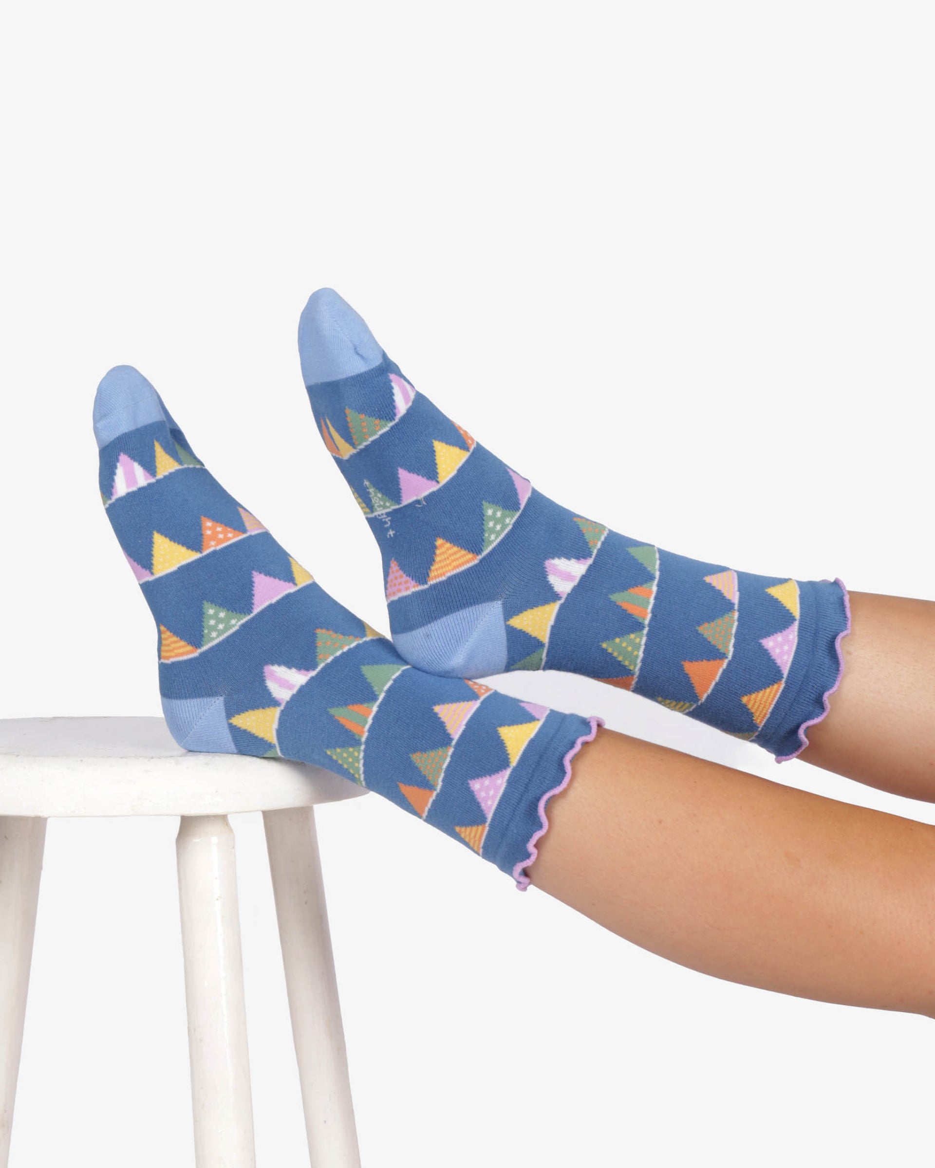 Colorful patterned socks worn by a person sitting on a white chair.