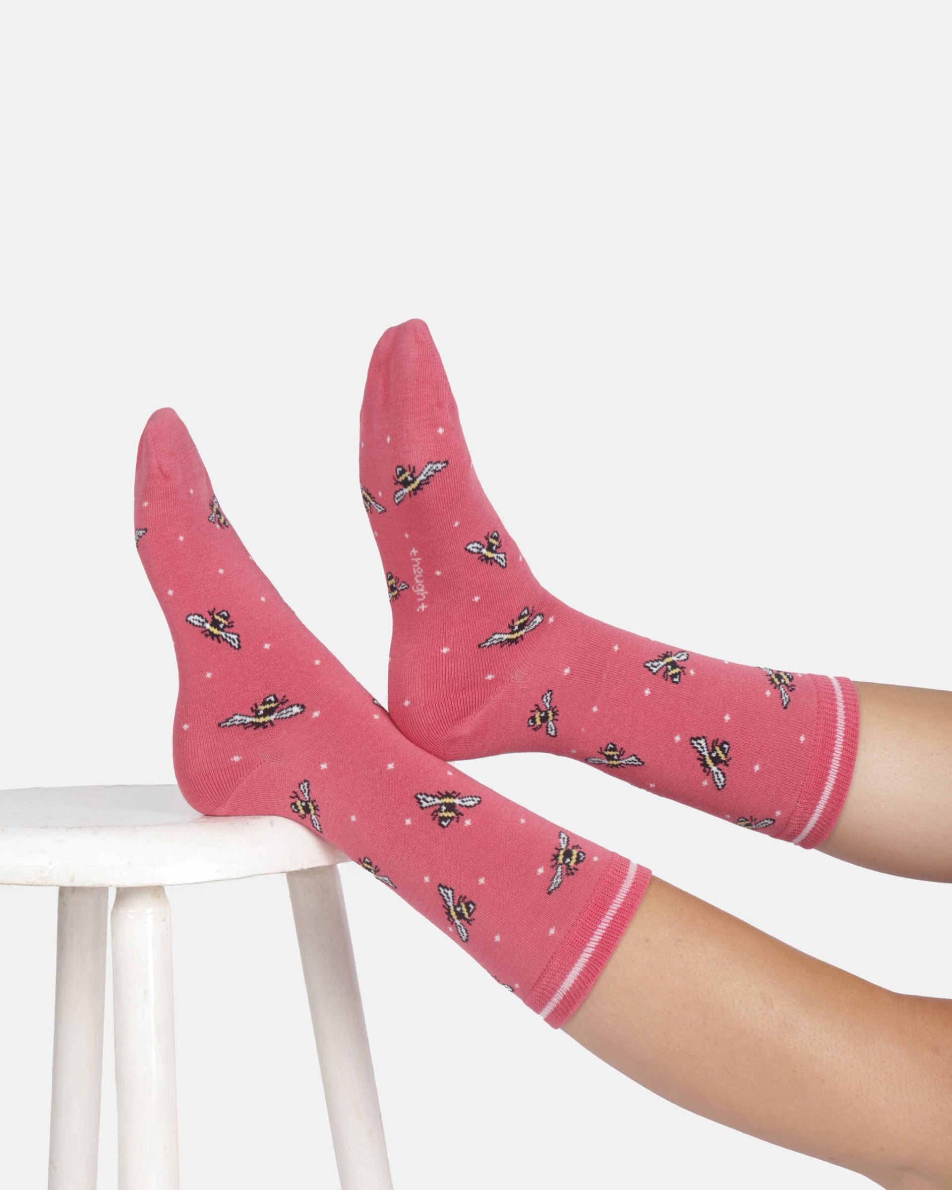 Pink socks with airplane pattern worn by a person on a white stool against a light gray background