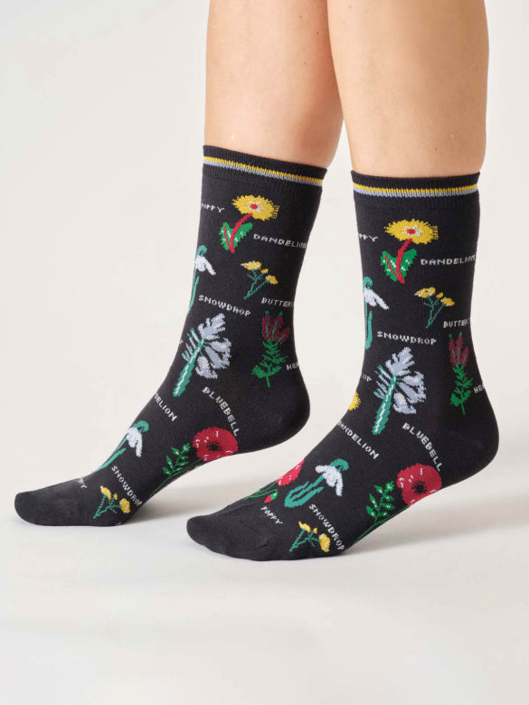 Black socks with colorful floral patterns worn by a person on a light gray background