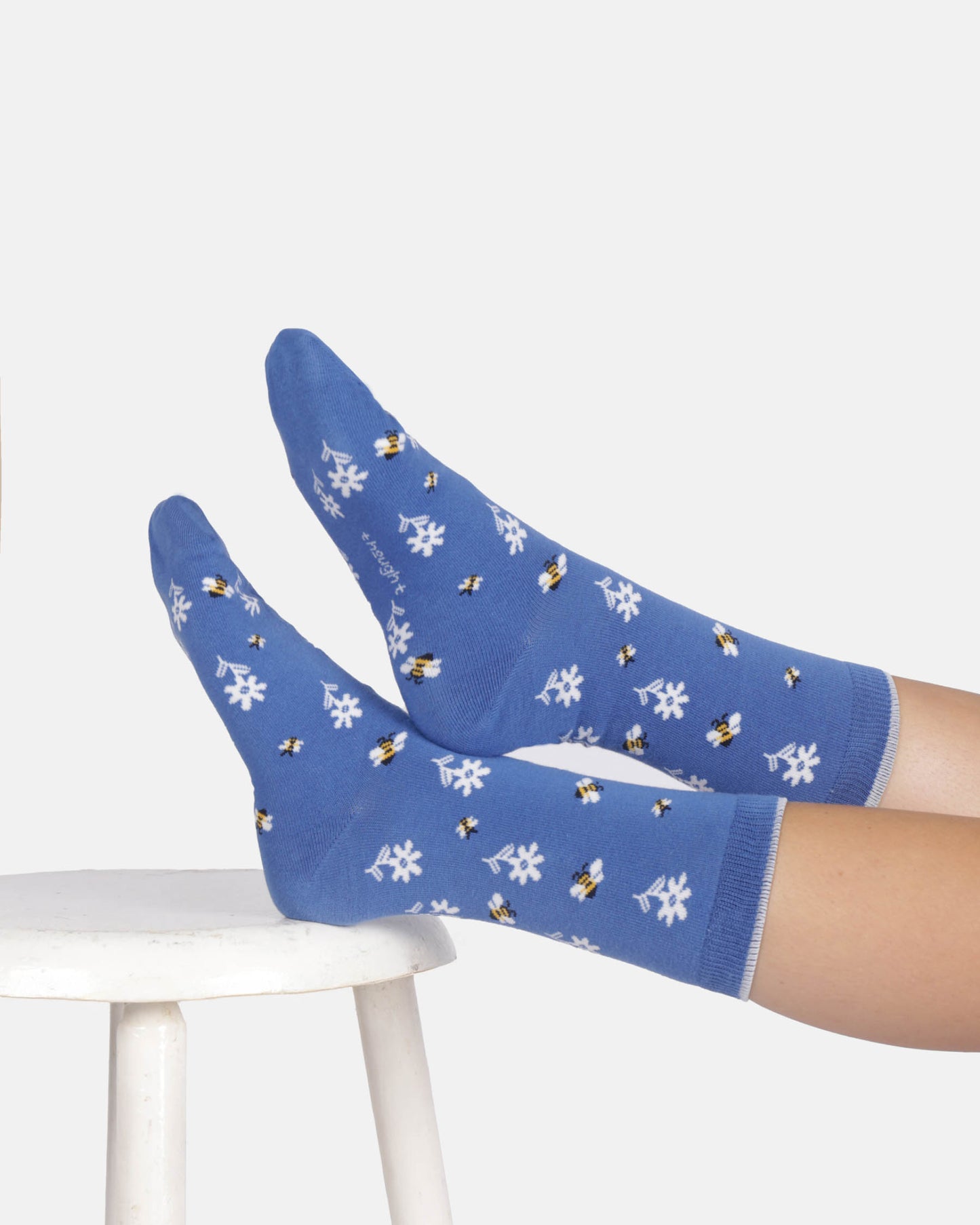 Blue socks with white floral and bee pattern worn by a person sitting on a white stool.