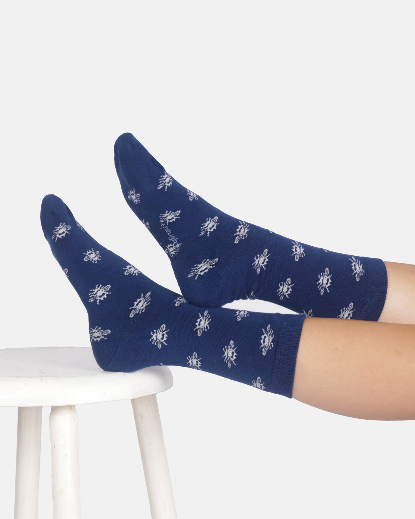 Navy blue socks with white bees patterns worn by a person sitting on a white stool.