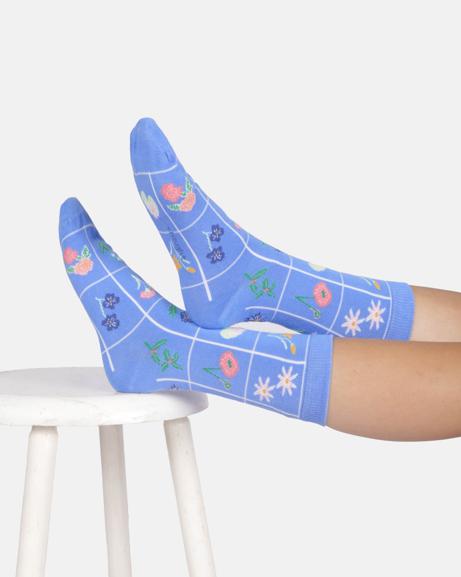 Blue floral-patterned socks worn by a person sitting on a white stool.