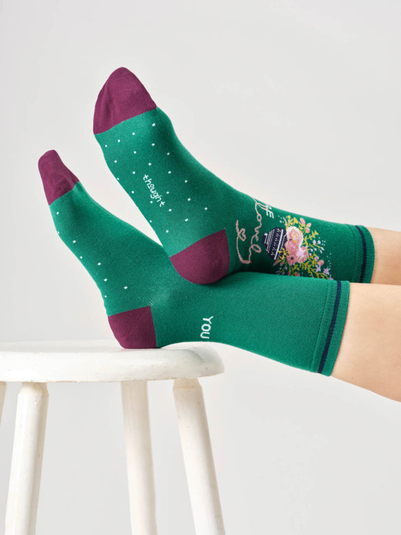 Green socks with purple accents worn by a person sitting on a white stool.