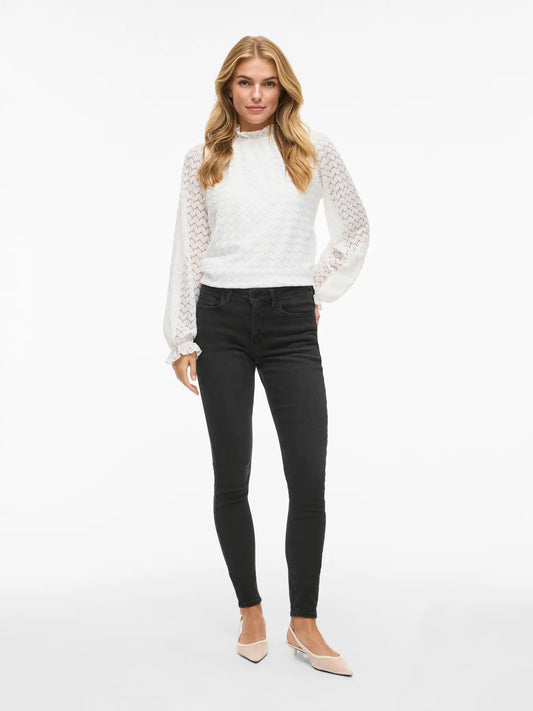 Woman wearing a white lace top and black jeans on a white background