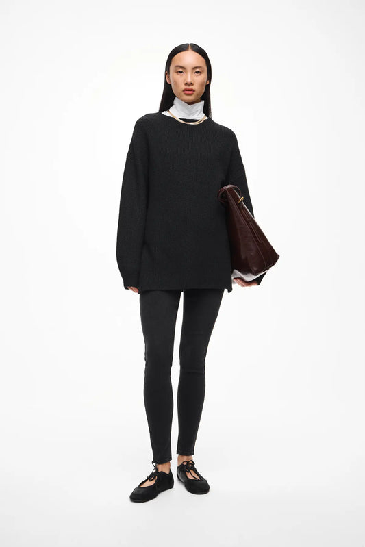 Person wearing a black outfit holding a brown bag on a white background