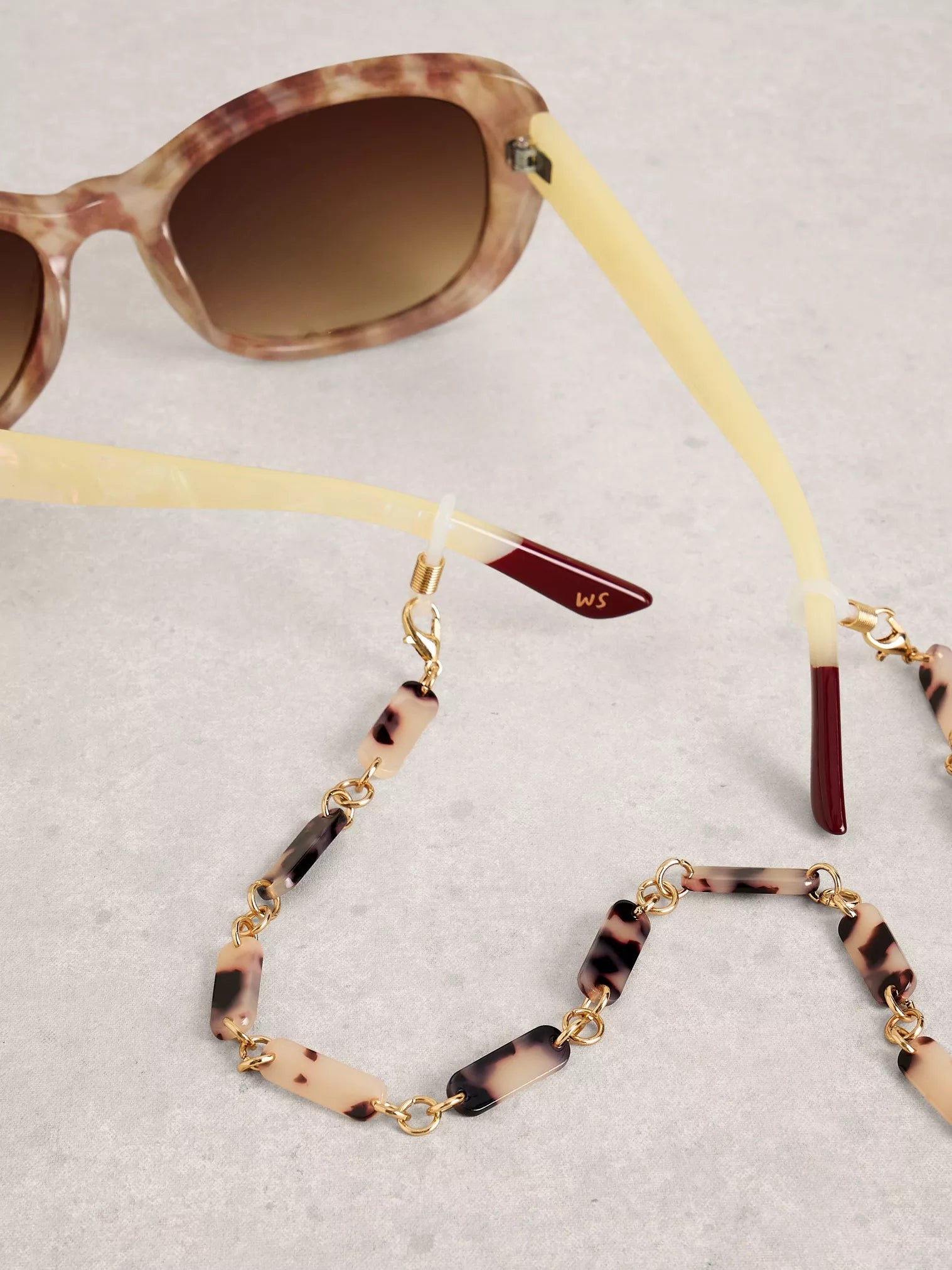Sunglasses with a tortoiseshell chain strap on a light gray background
