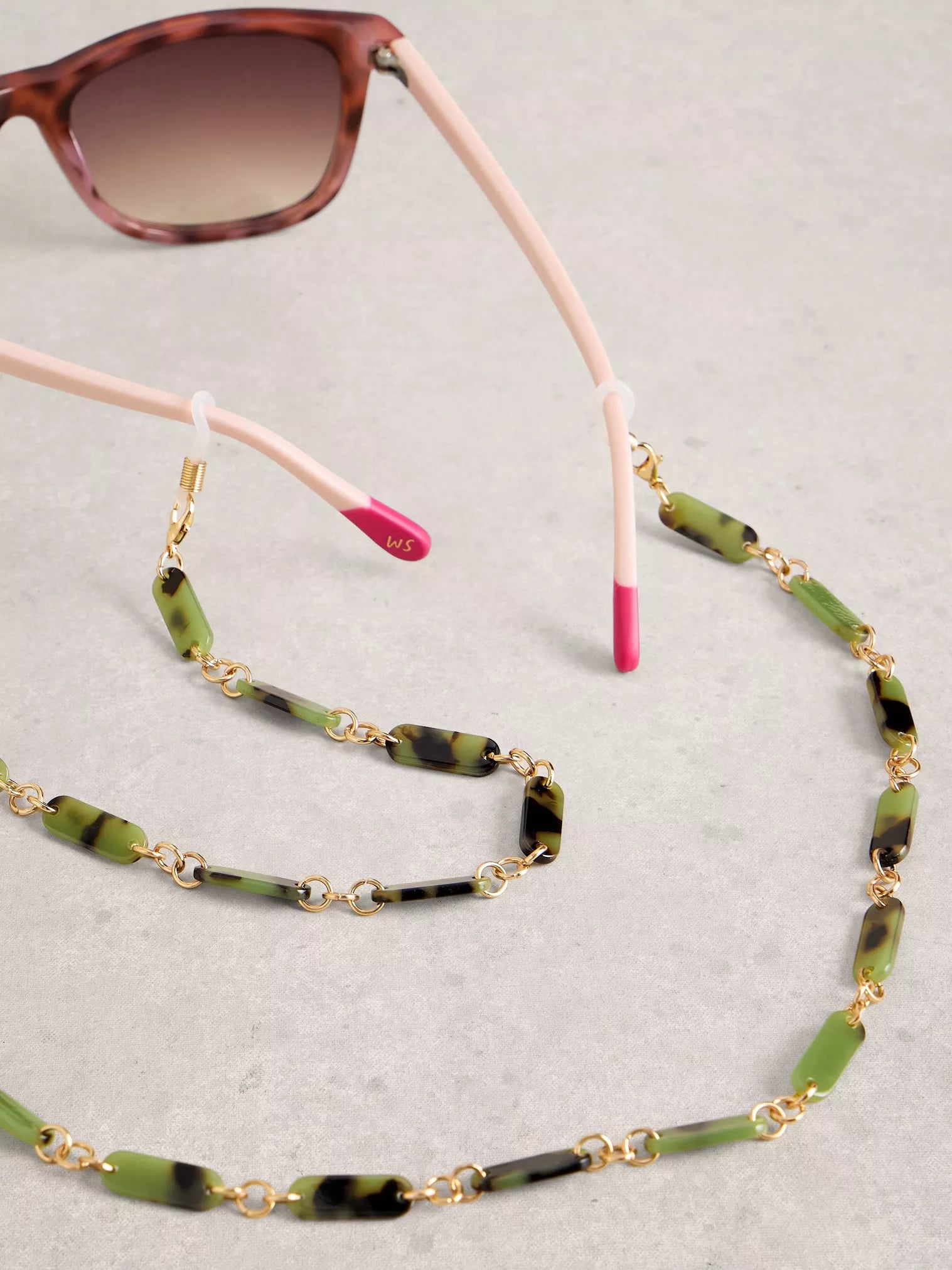 Green and gold beaded eyeglass chain with sunglasses on a gray background