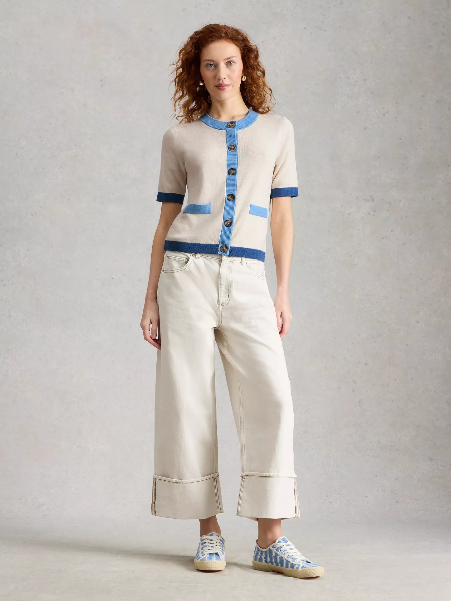 Woman wearing a cream and blue outfit with wide-leg pants on a gray background