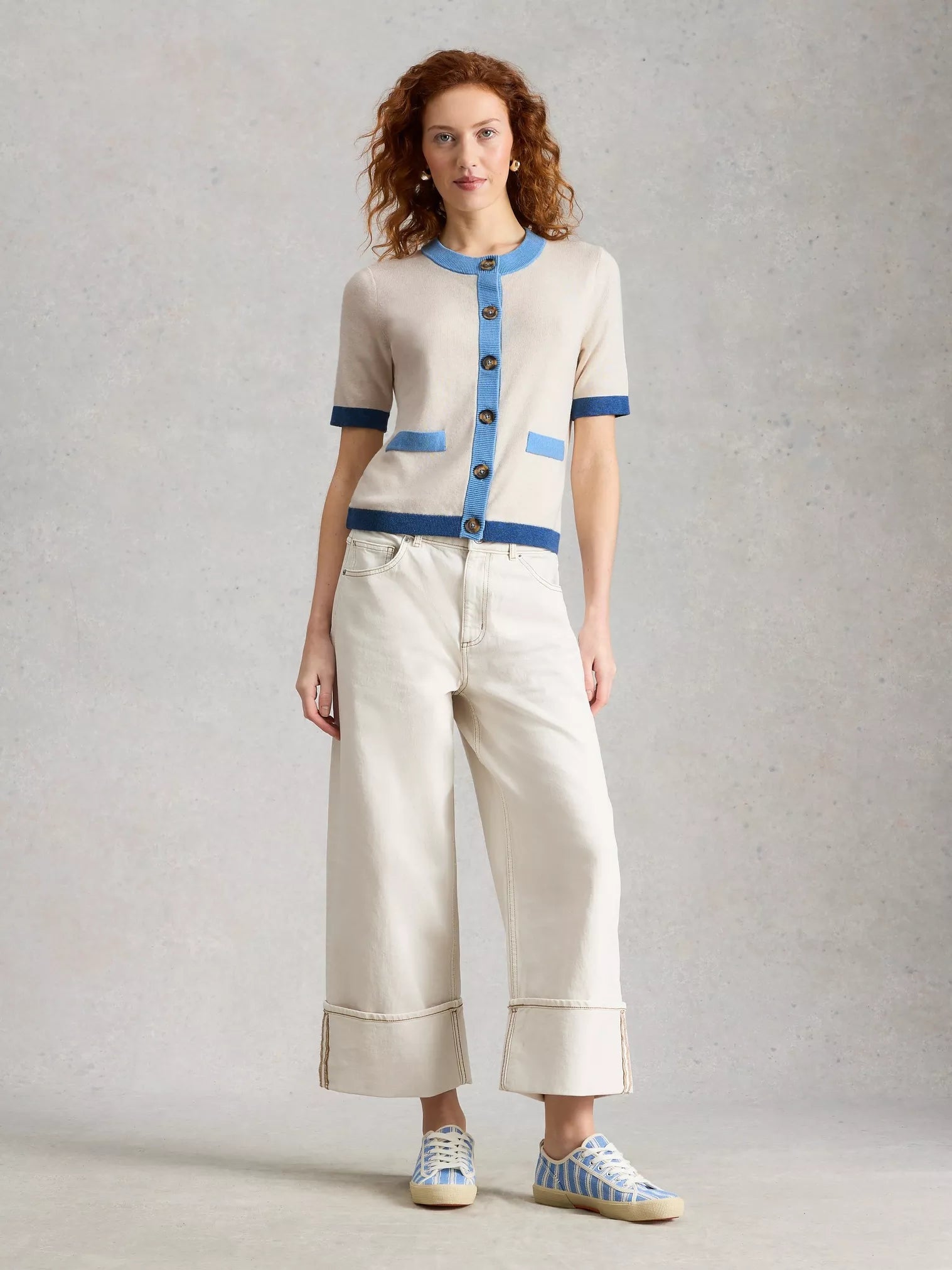 Woman wearing a cream and blue outfit with wide-leg pants on a gray background