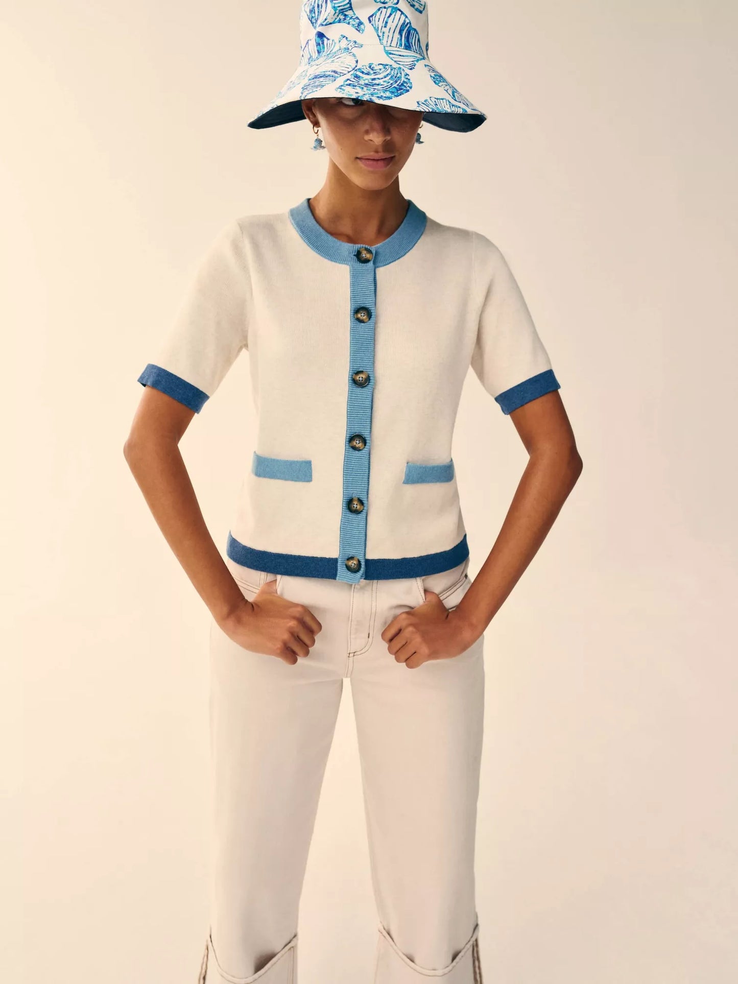 Person wearing a white cardigan with blue accents and a matching hat on a plain background