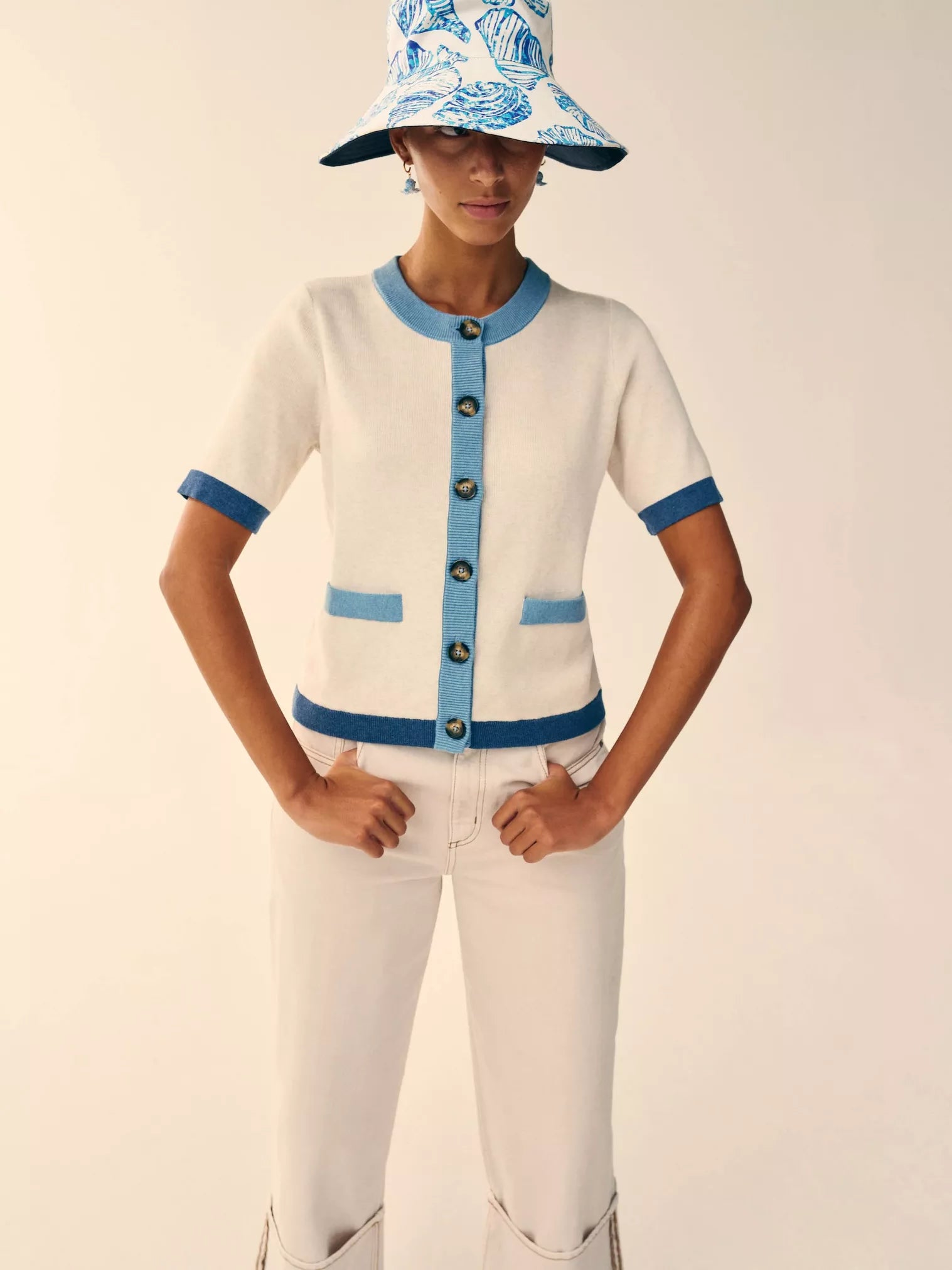 Person wearing a white cardigan with blue accents and a matching hat on a plain background