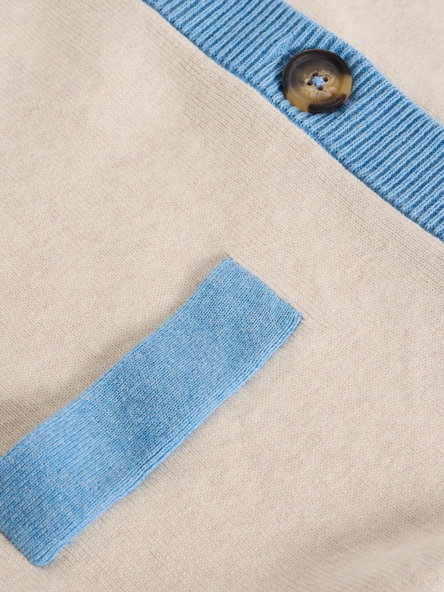 Close-up of a beige fabric with blue trim and a button, on a beige background.