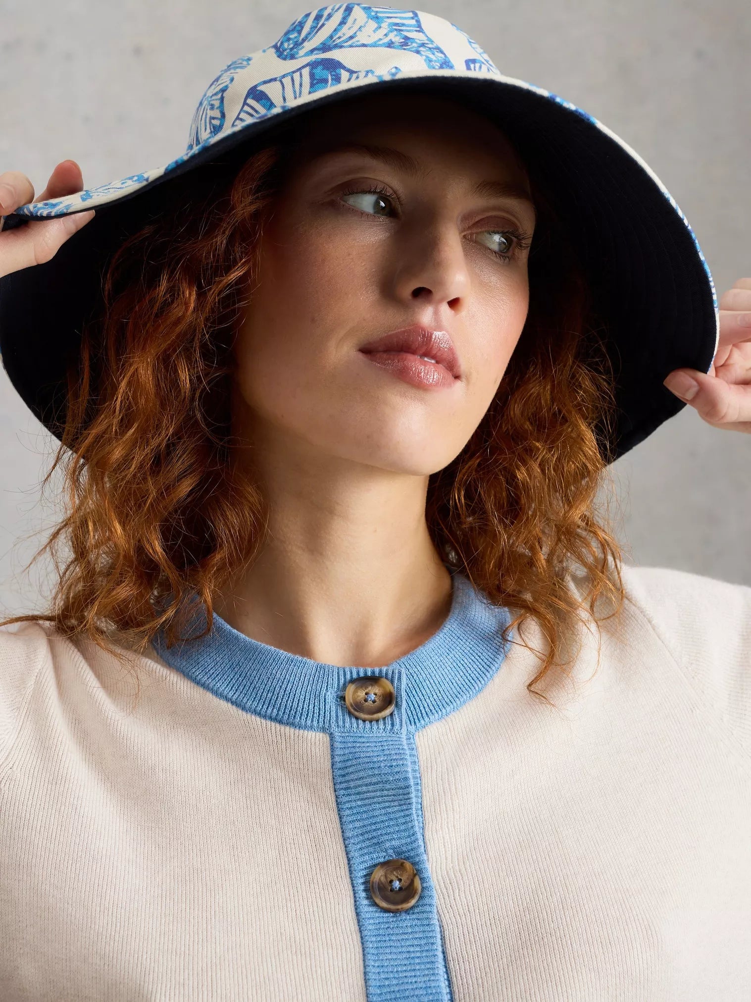 Woman wearing a patterned bucket hat and beige outfit with blue accents.