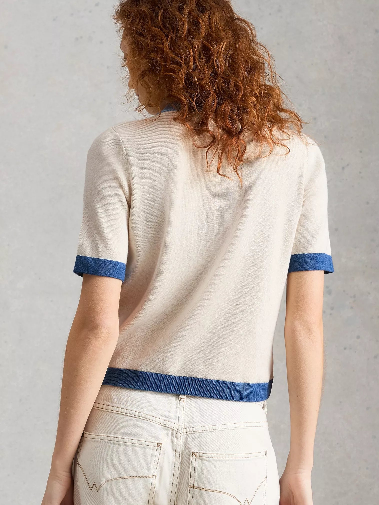 Person wearing a white sweater with blue trim against a gray background