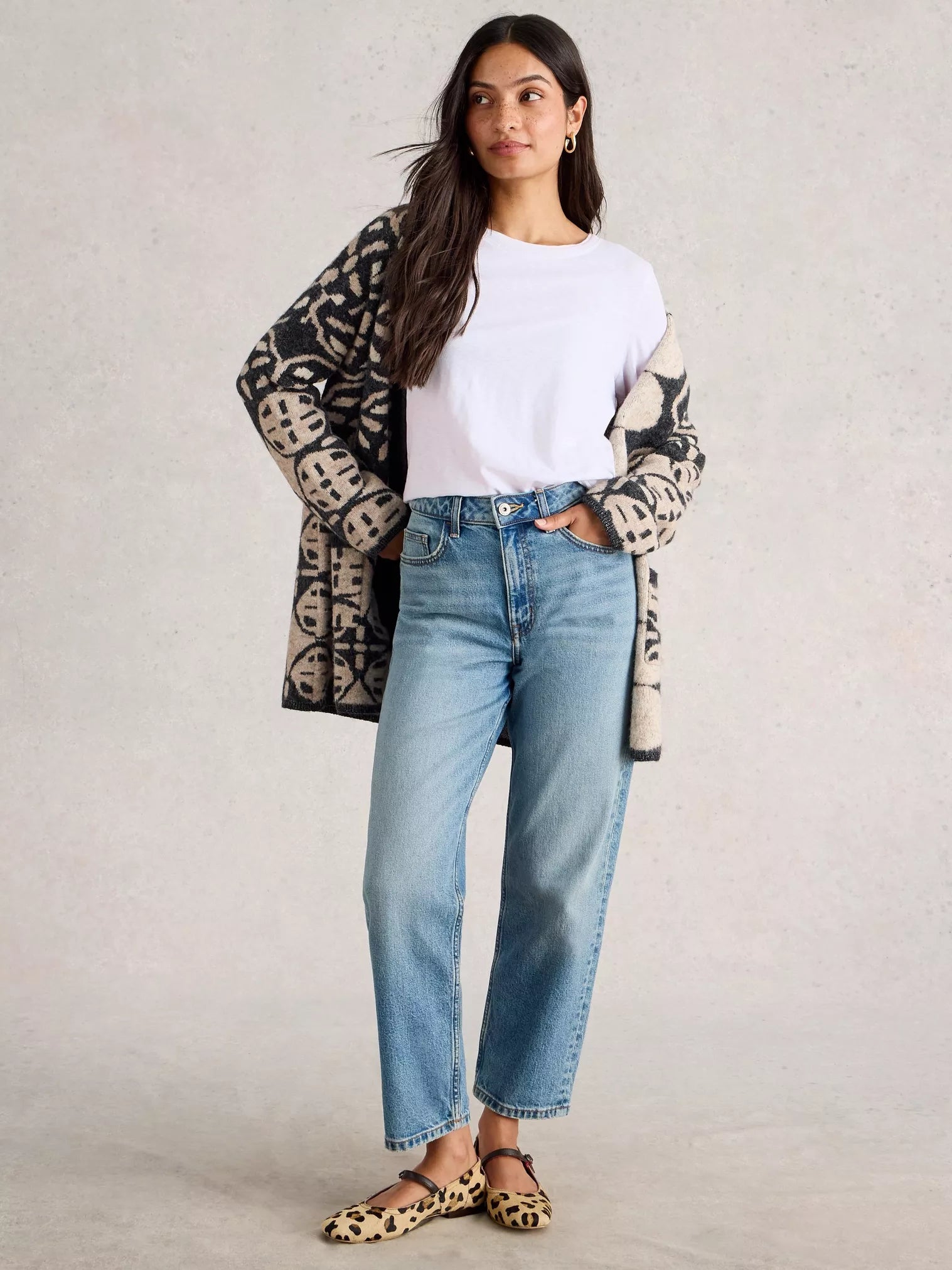 Woman wearing a patterned cardigan, white shirt, blue jeans, and leopard print shoes on a plain background