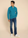 Man wearing a teal sweater and blue jeans against a beige background