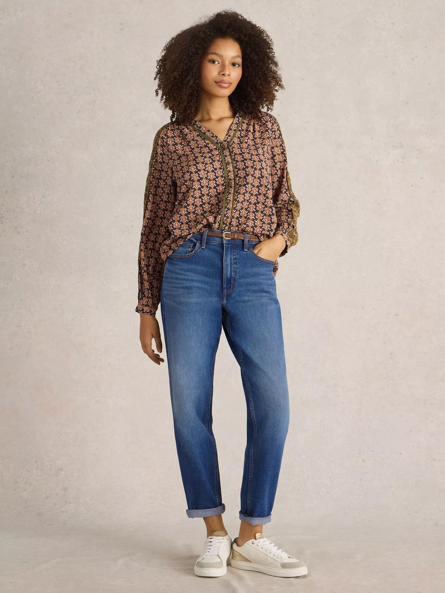 Woman wearing a patterned blouse and blue jeans against a plain background