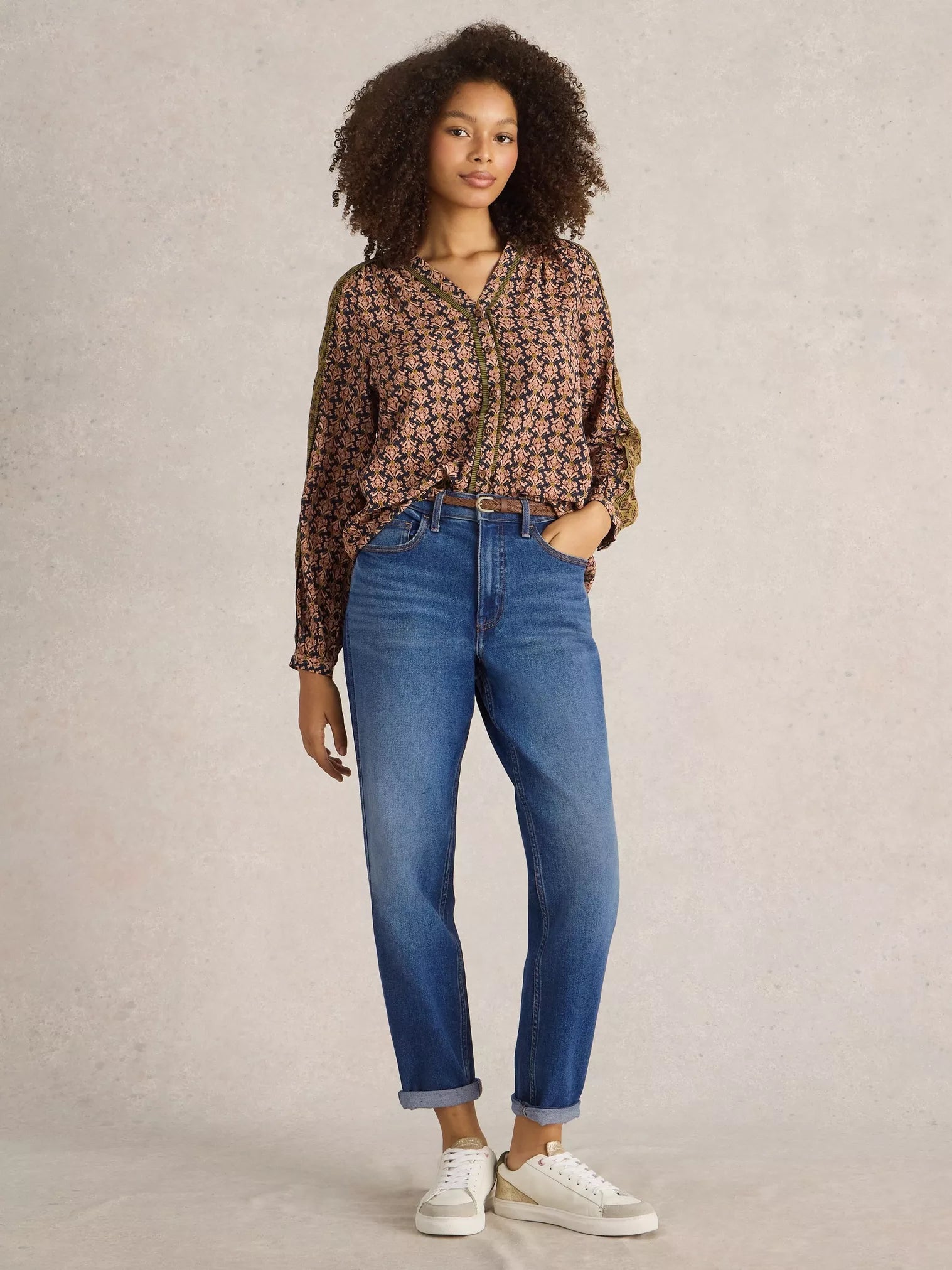 Woman wearing a patterned blouse and blue jeans against a plain background