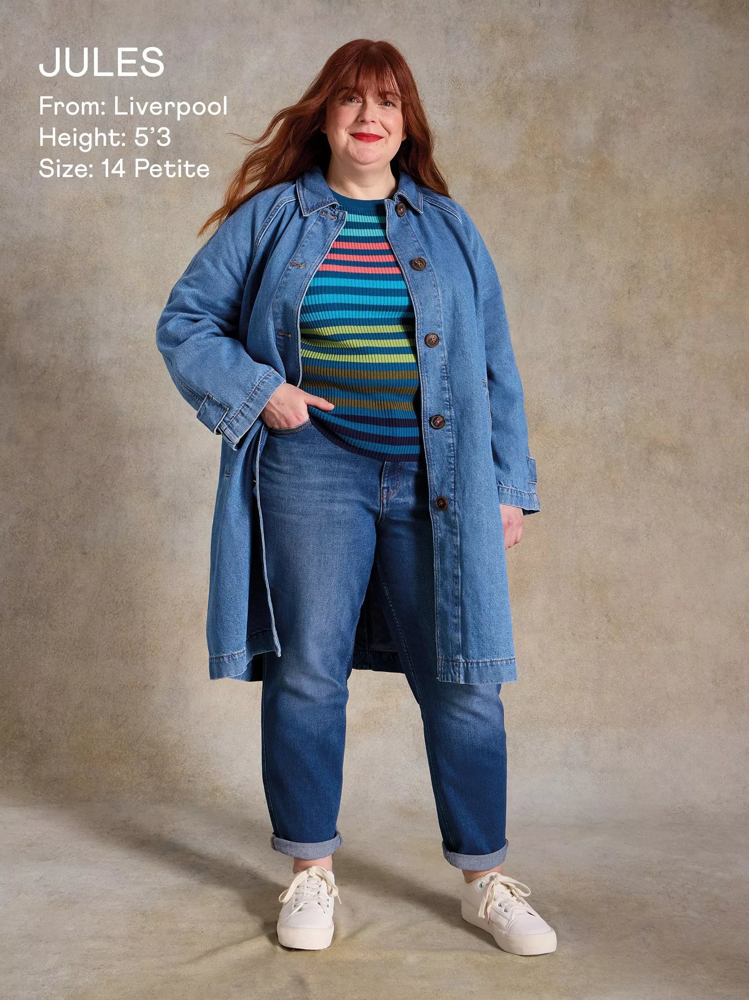 Woman wearing a blue denim jacket and jeans with a striped shirt, standing against a plain background.