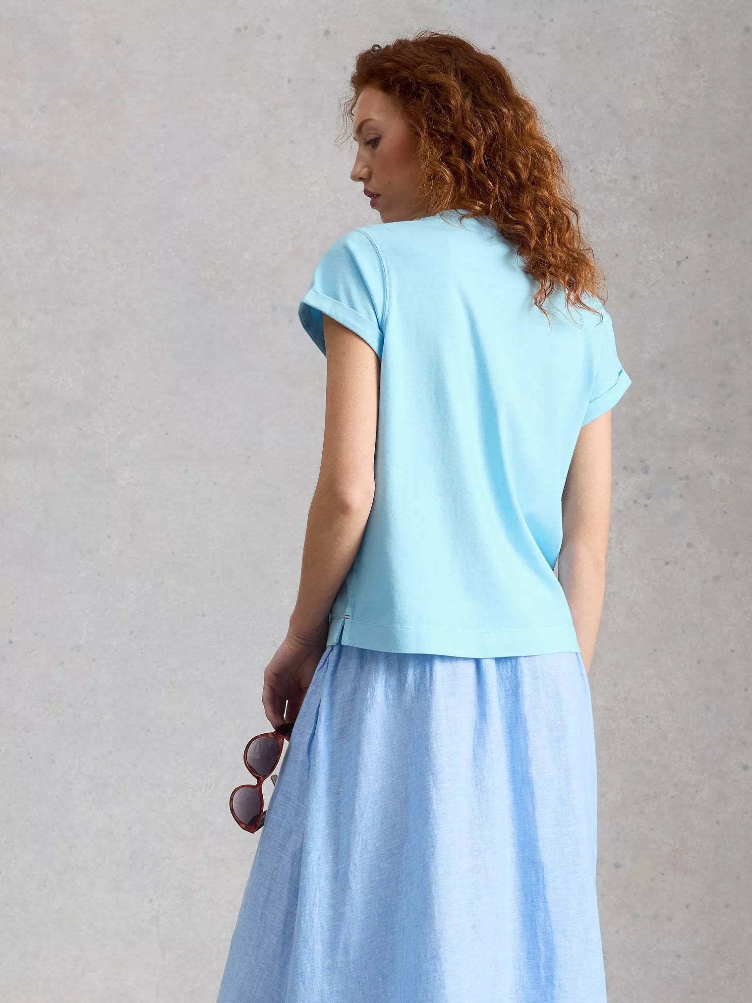 Woman wearing a light blue top and skirt against a gray background