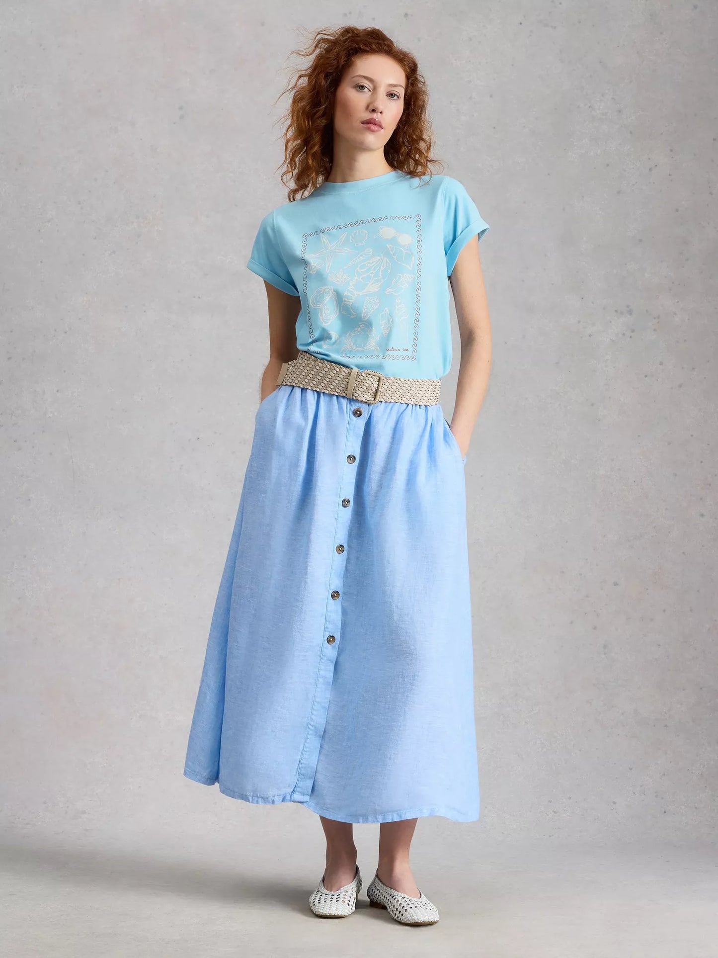 Woman wearing a light blue t-shirt and denim skirt against a plain background