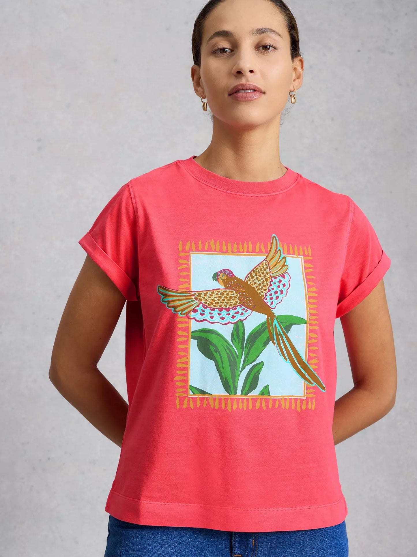 Person wearing a pink t-shirt with a bird and plant design on a gray background