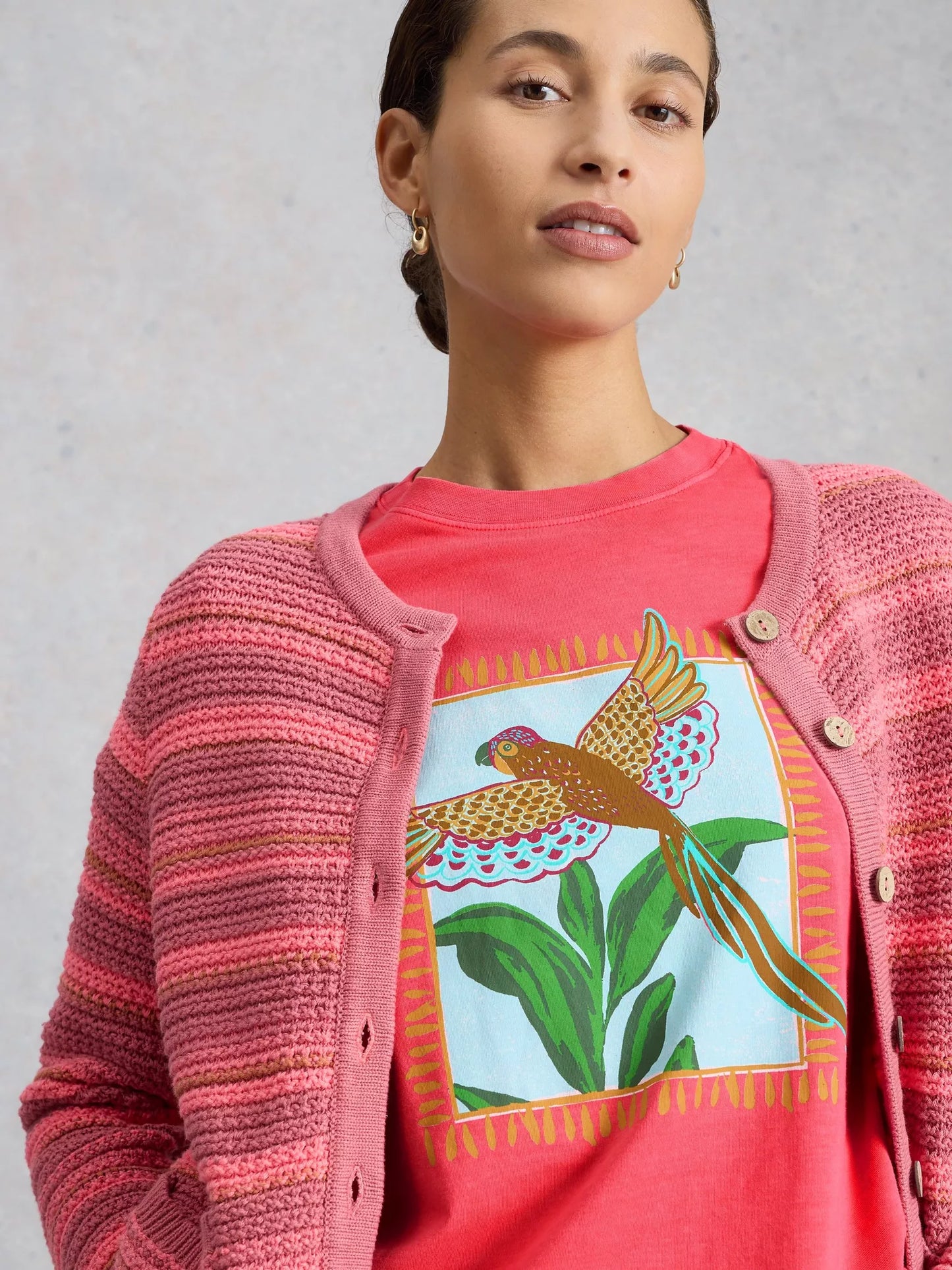 Woman wearing a pink cardigan over a red shirt with a colorful bird design.