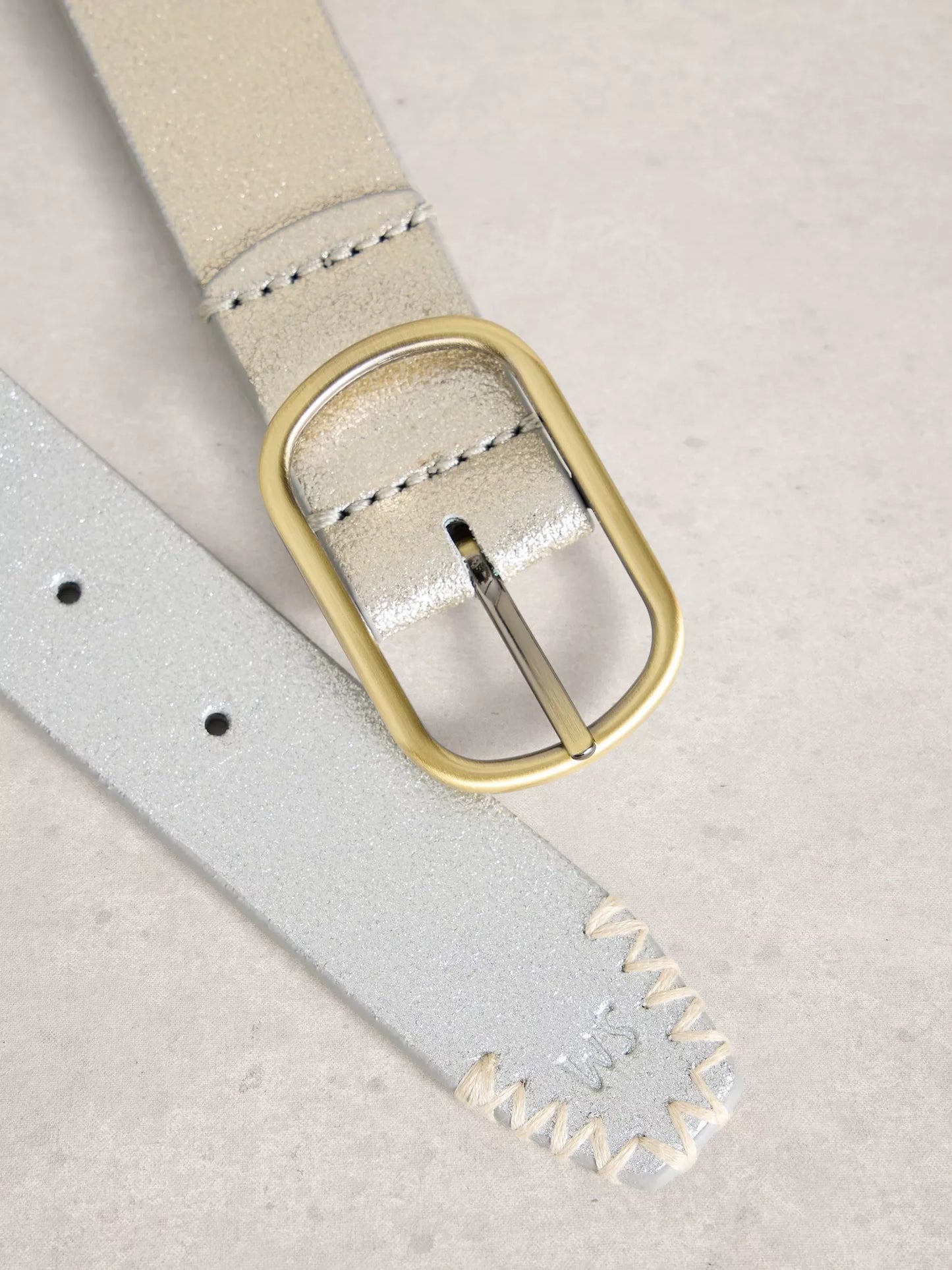 Close-up of a beige suede belt with a gold buckle on a light gray background