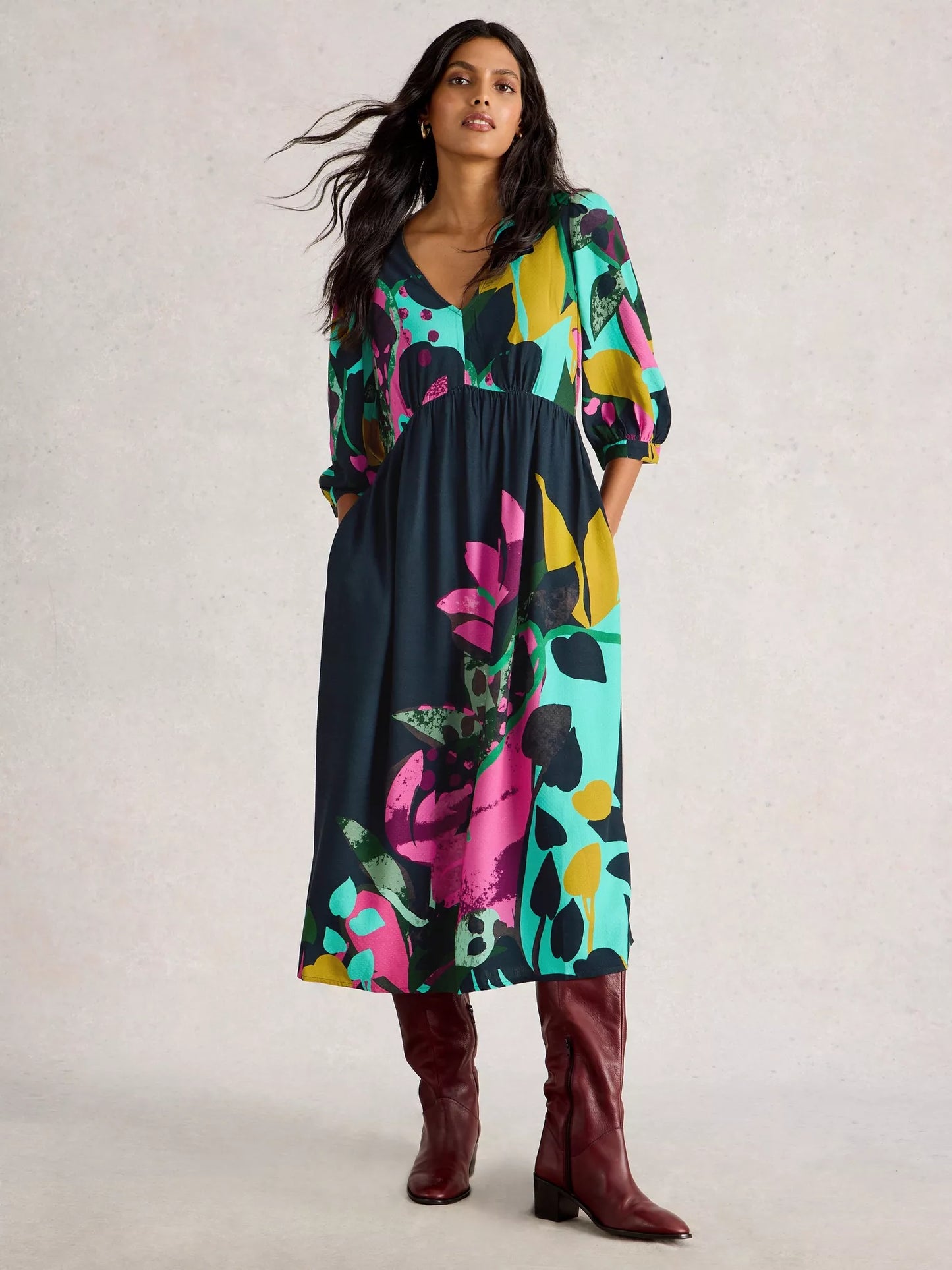 Woman wearing a colorful floral dress with brown boots on a light background