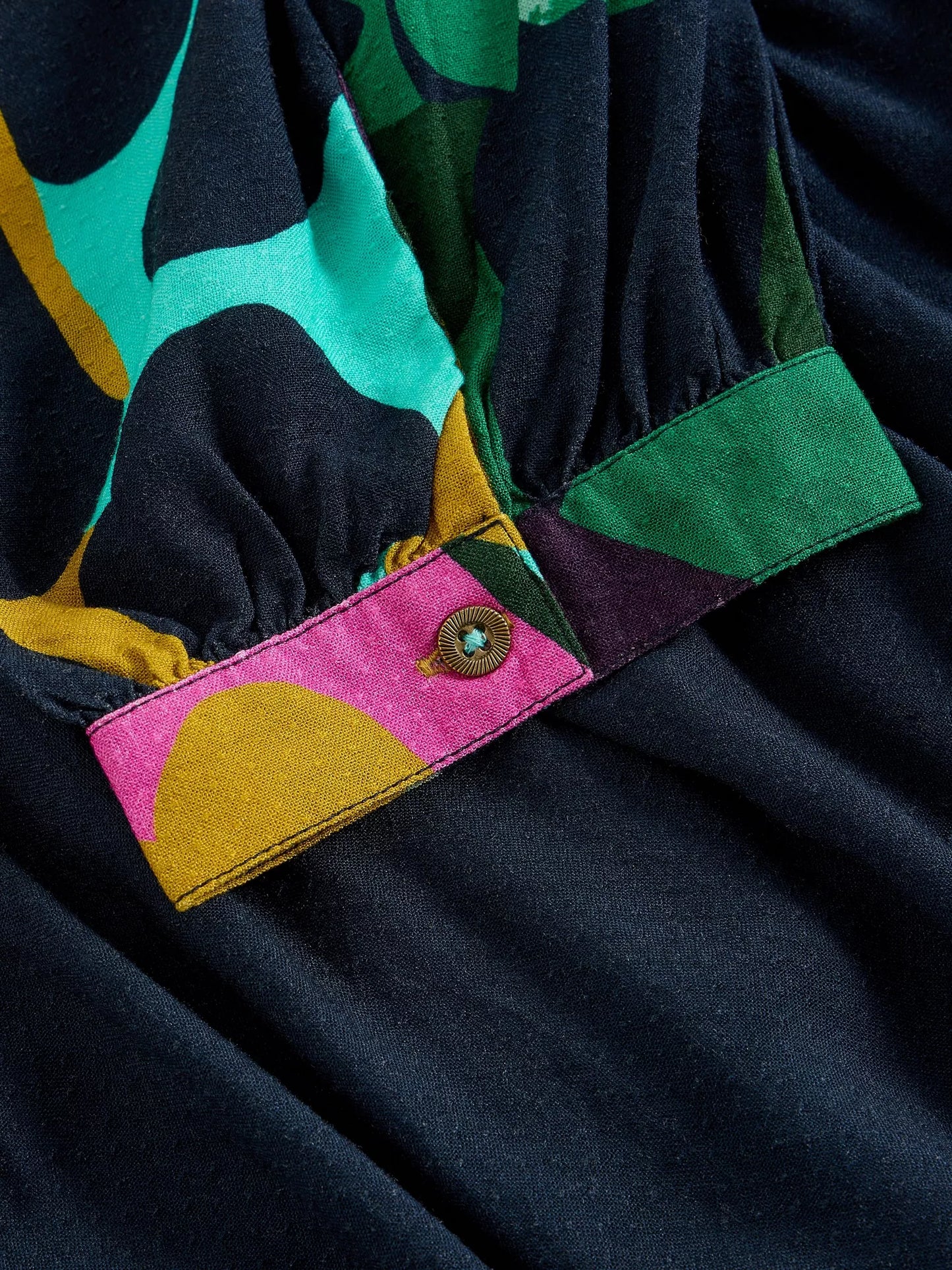 Close-up of a colorful fabric with a pink patch featuring a yellow half-circle and green button.