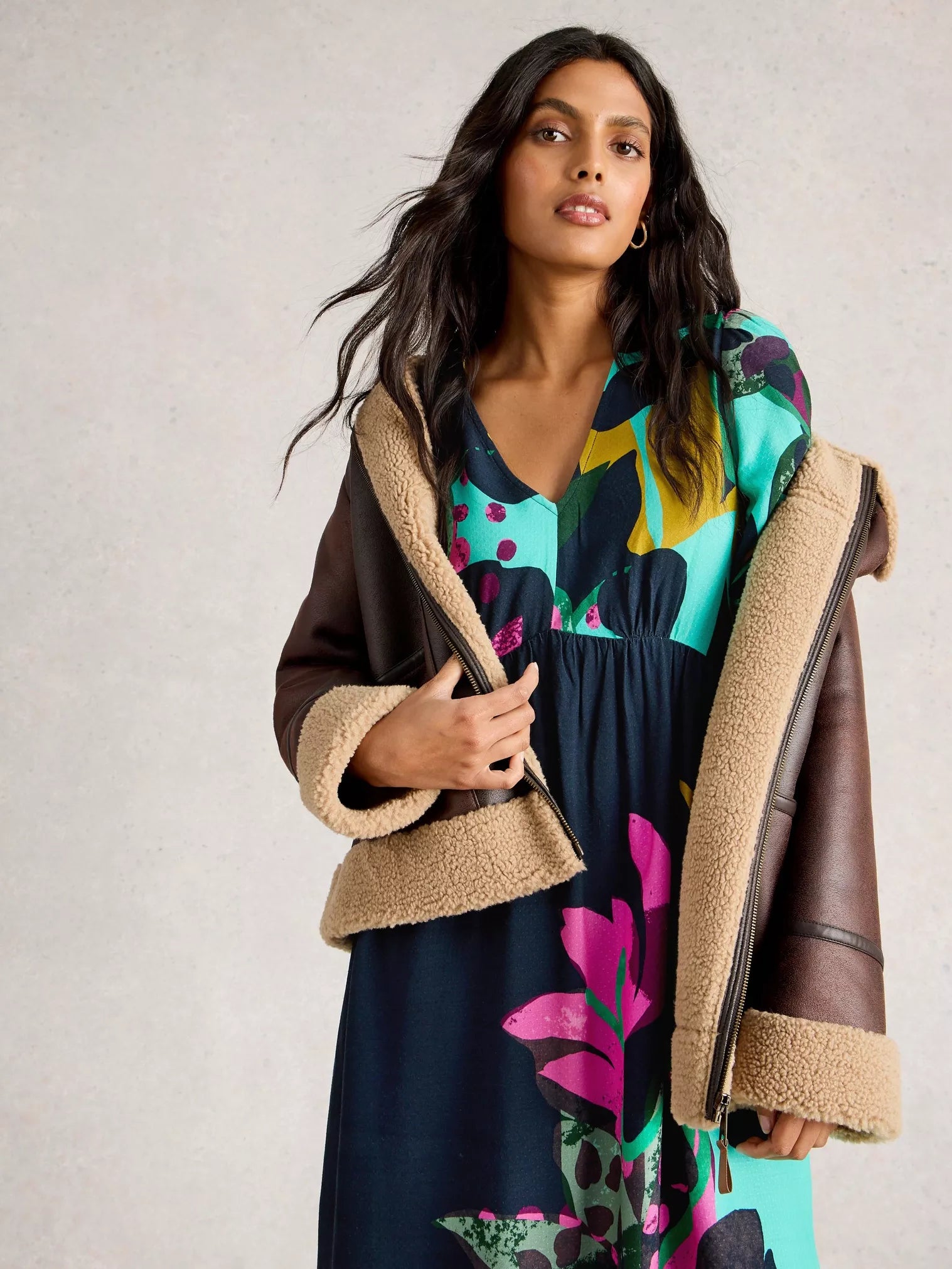 Woman wearing a colorful dress with a brown shearling jacket against a neutral background