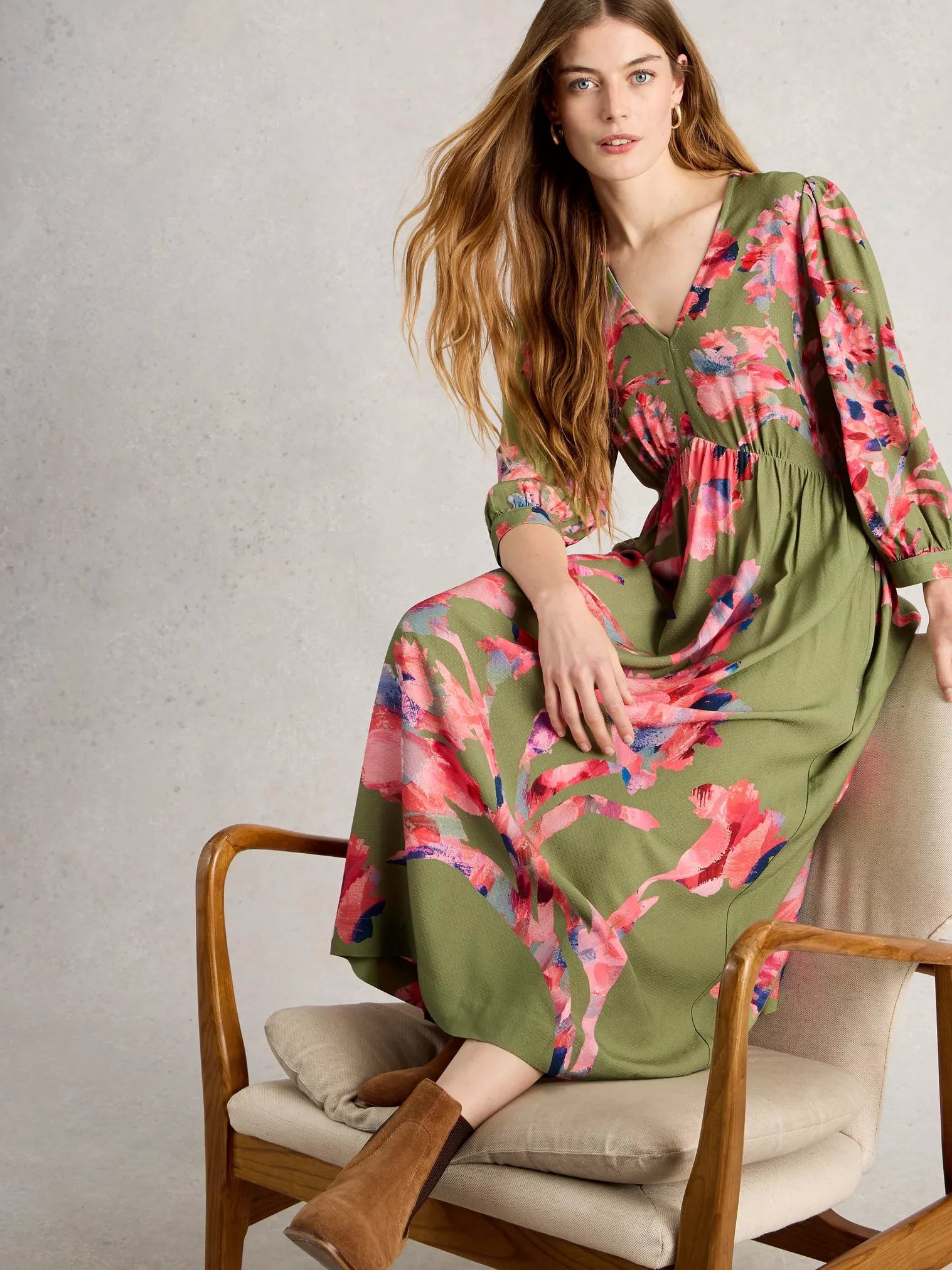 Woman wearing a floral dress sitting on a chair with a neutral background