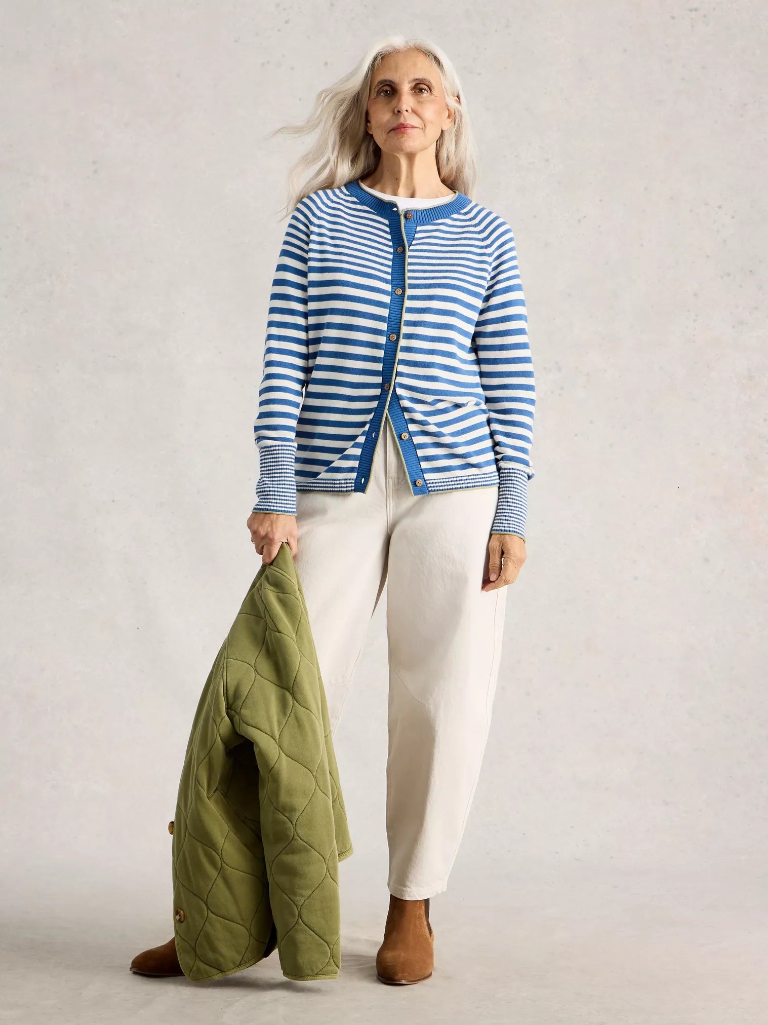 Lady wearing striped cardigan with neutral jeans and holding green jacket