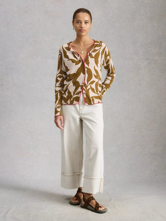 Woman wearing a patterned top and white pants against a plain background