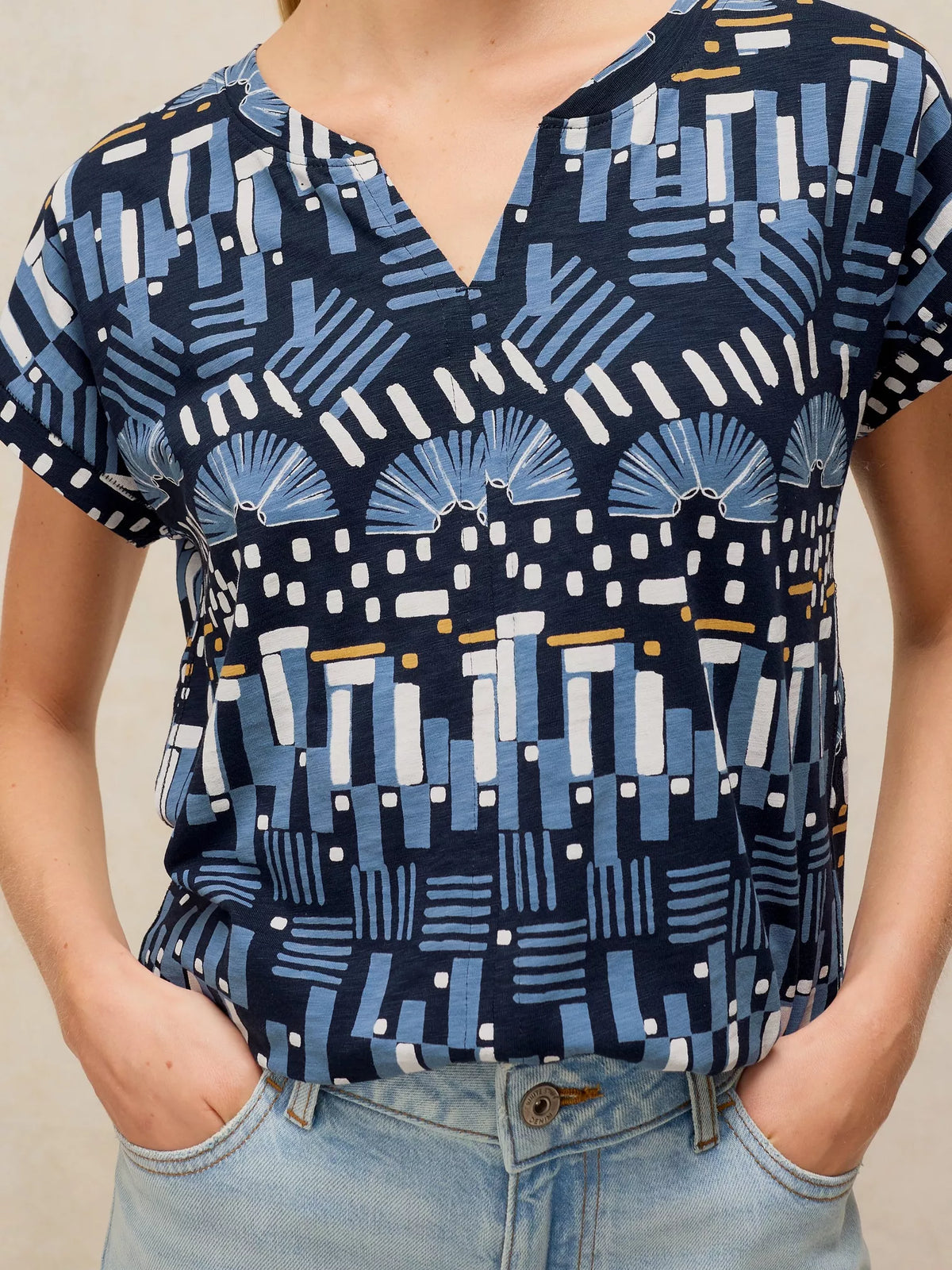 A woman wearing a short-sleeve V-neck top with a navy blue, light blue, and white geometric pattern, paired with light-wash blue jeans.