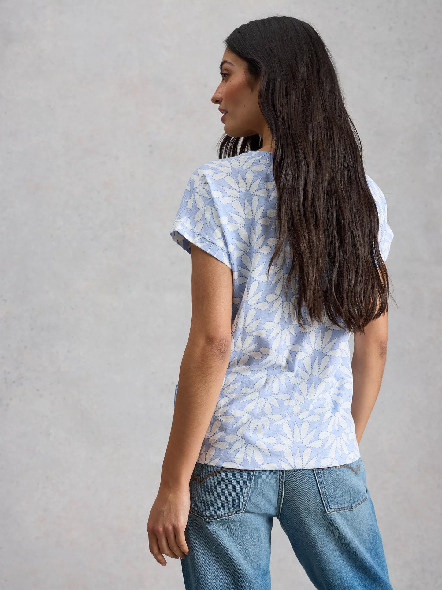 Woman wearing a light blue floral patterned shirt and jeans against a gray background