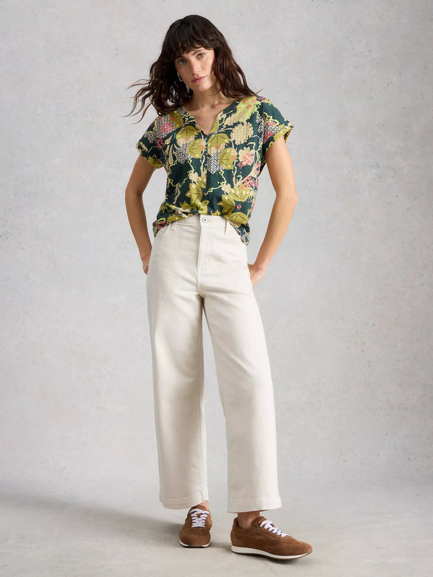 Woman wearing a floral shirt and white pants against a plain background