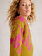 Woman wearing a mustard yellow dress with pink floral pattern against a plain background