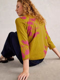 Woman wearing a mustard yellow sweater with pink floral patterns sitting on the floor.