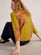 Woman wearing a mustard yellow sweater with pink floral patterns sitting on the floor.