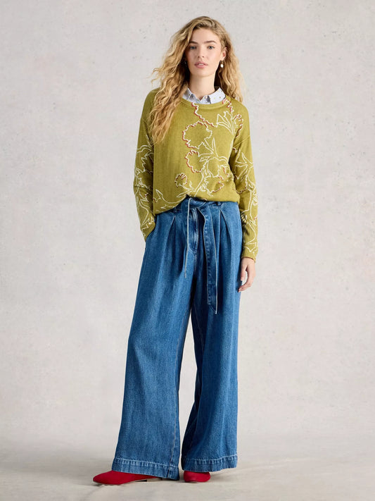 Woman wearing a green patterned jumper and blue jeans on a plain background