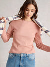 Woman wearing a pink long-sleeve top and blue jeans, holding a striped blanket.