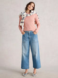 Woman wearing a pink sweater, blue jeans, and a patterned scarf on a plain background